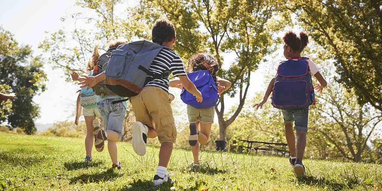 Bambini corrono su un prato all’uscita da scuola: anche le scuole possono essere esempi di sostenibilità