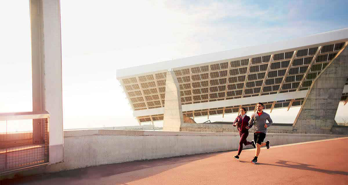 Due persone si allenano correndo in un impianto sportivo moderno: le nuove strutture sono attente alla riqualificazione energetica