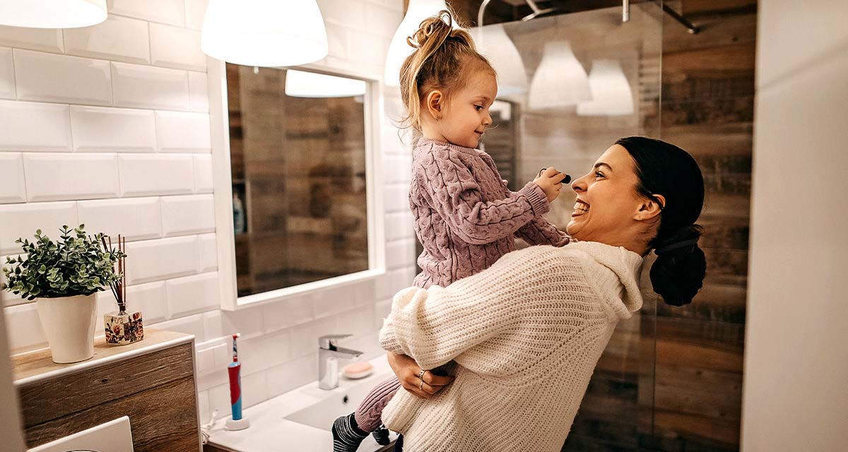 Una mamma gioca con la figlia piccola in braccio in un bagno luminoso