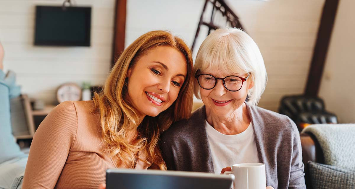 Due donne sorridono mentre consultano un tablet insieme, in un momento di condivisione e relax domestico