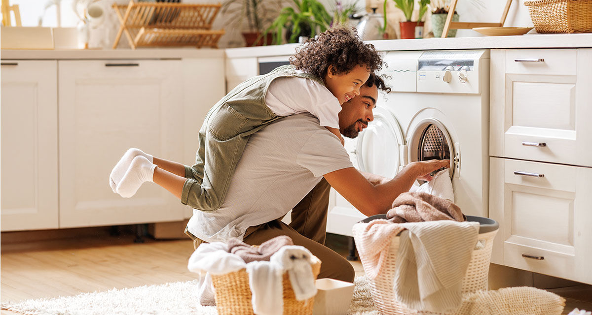 Un papà e un bambino preparano una lavatrice, programmando l’orario più conveniente secondo la tariffa