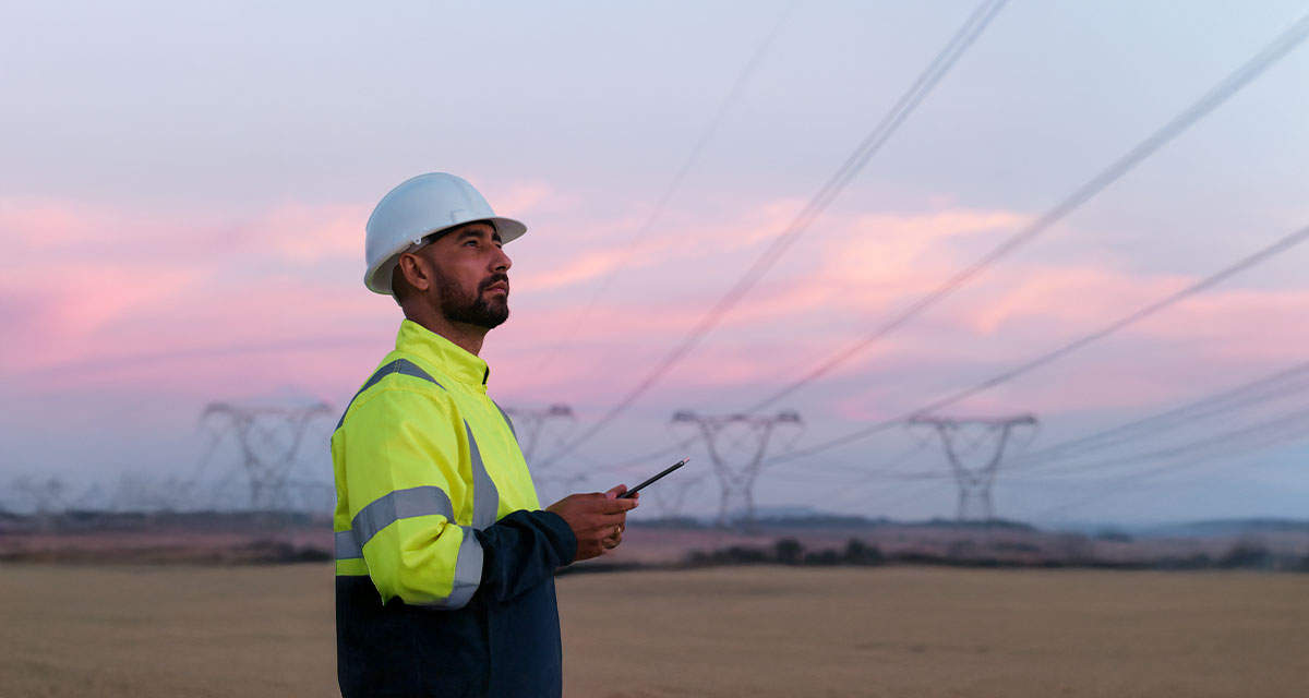 Un tecnico con le linee dell’alta tensione sullo sfondo: il dispacciamento assicura l’equilibrio della rete elettrica