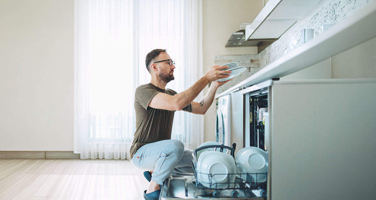 Un giovane uomo carica la lavastoviglie: utilizzarla a pieno carico riduce i consumi elettrici