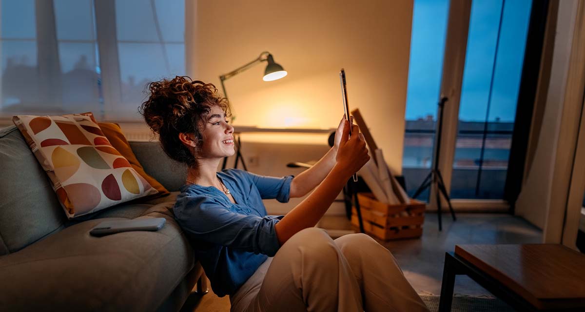 Una ragazza controlla il telefono in soggiorno: per scegliere le offerte energetiche migliori si può calcolare in autonomia il preventivo luce e gas