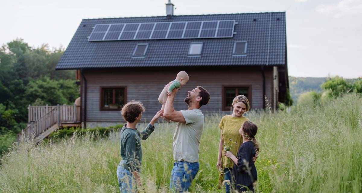 Mamma, papà e due bambini giocano accanto a una casa di campagna con impianto fotovoltaico professionale, preferibile rispetto al fotovoltaico fai da te